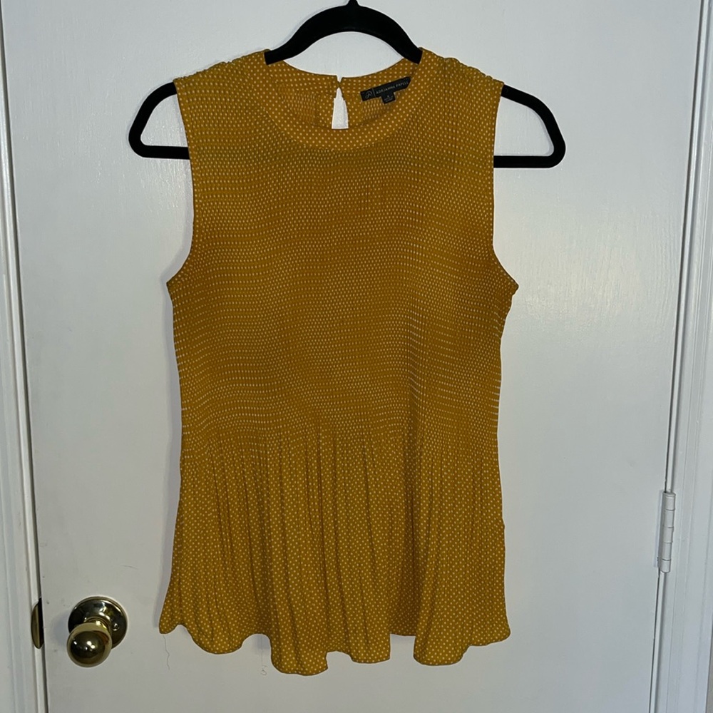 Mustard sleeveless stretch form fitting pleated white polka dot pattern top.